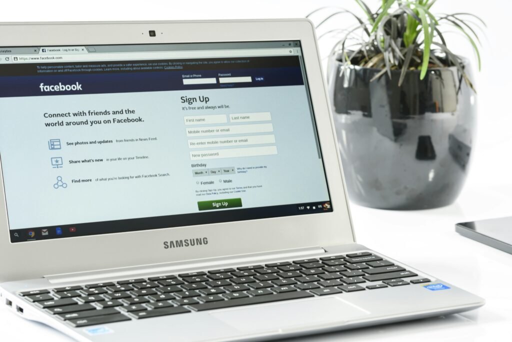 FLORIDA BUSINESS HUB LLC Open Samsung laptop showing Facebook sign-up page next to a potted plant. Ideal for technology themes.